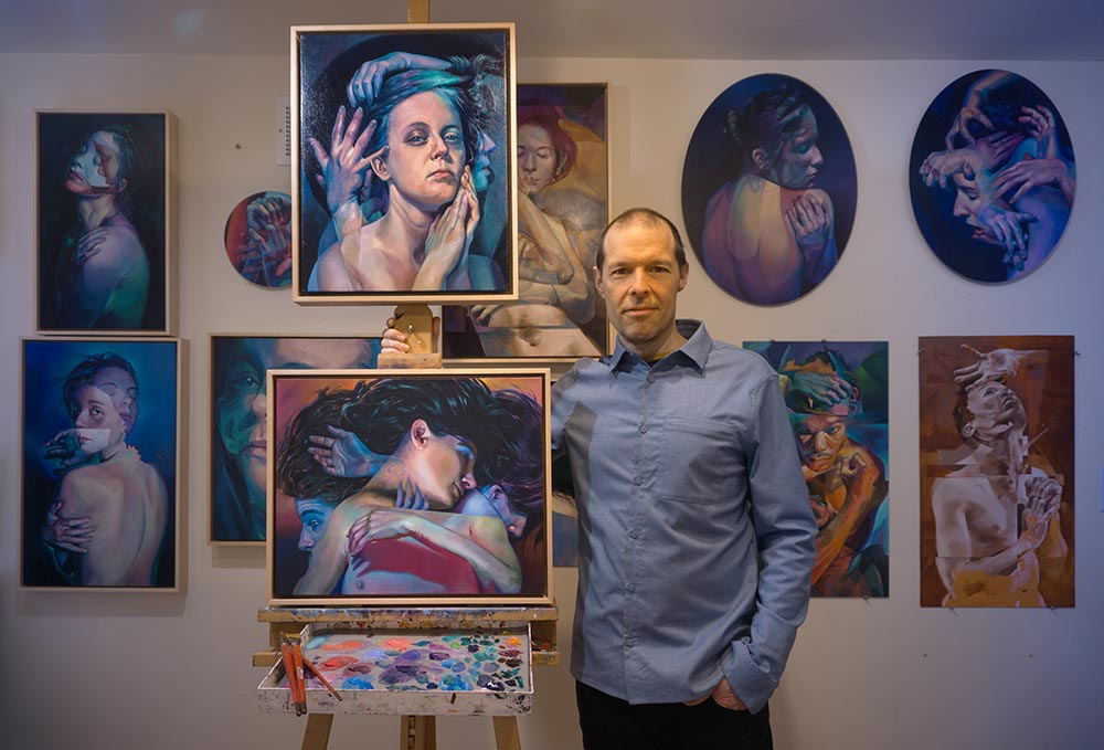 Scott Hutchison standing next to two of his paintings in his studio